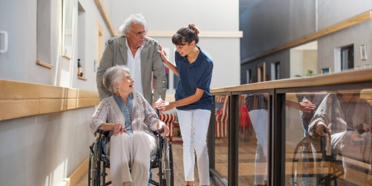 Nursing Staff Assisting an Elderly Couple in a Hallway at an Assisted Living Facility
