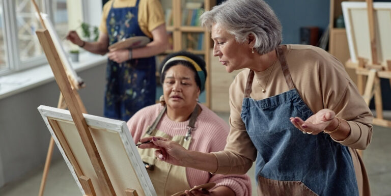 Elderly Woman Teaching Another Resident How to Paint at an Independent Living Facility.